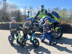 Dzieci na rowerach, w tle Policjant Wydziału Ruchu Drogowego KPP Dębica z motocyklem służbowym